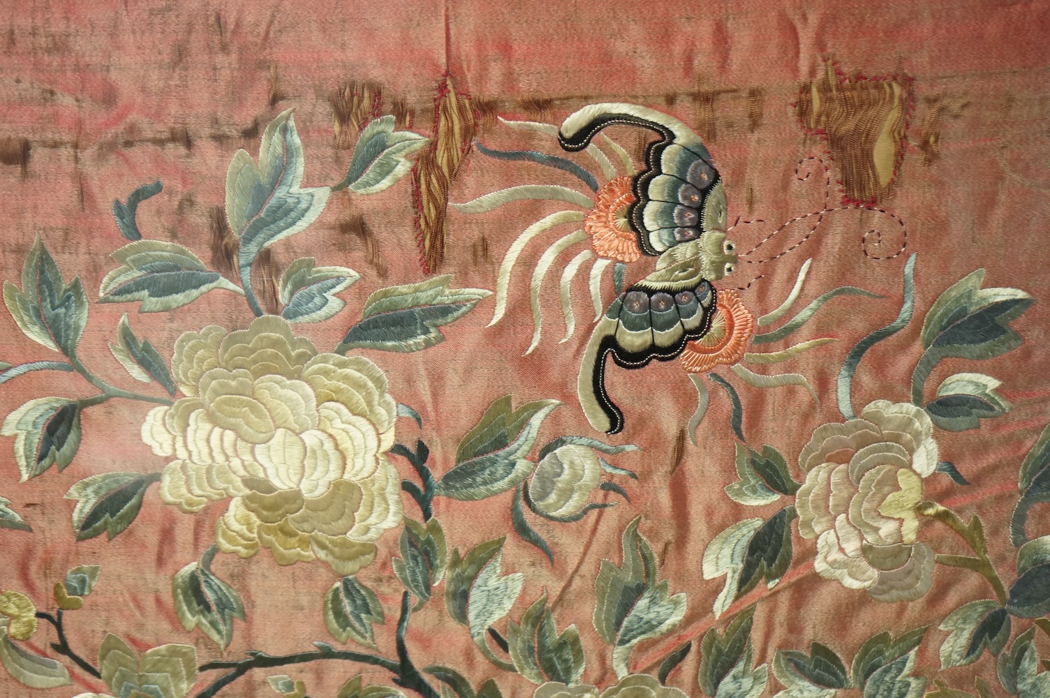 A pair of framed early 20th century Chinese silk embroideries, probably panels cut from a larger embroidery or bed cover. Embroidered with a large central cartouche of flowers birds and butterflies. 89cm x 73cm. Conditio